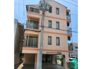 3階建てのオレンジ色の介護施設外観。1階に駐車場、各階にバルコニー付き